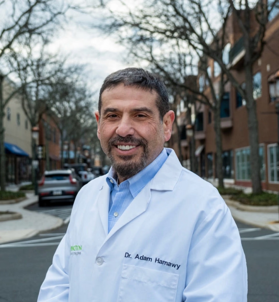 Portrait photo of Adam Hamawy in a medical jacket, with a neighborhood in the background.
