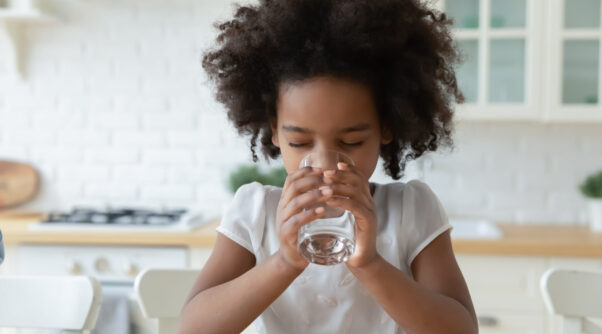 Photo of an african-american child sitting down and drinking a glass of water.