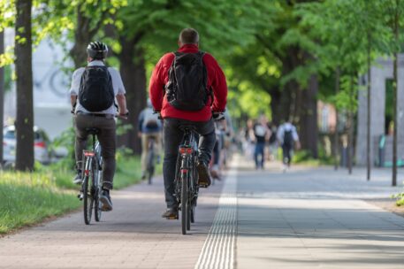 Male,Cyclists,With,Backpacks,On,Bike,Path,In,Avenue Two people with backpacks riding their bikes in a designated lane during the afternoon.